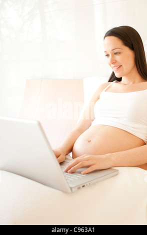 Pregnant woman using a laptop in bed. Stock Photo