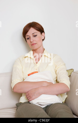 Abdominal pain. Woman holding a hot water bottle over her abdomen. Stock Photo