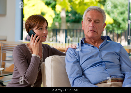 Senior man having a stroke. He is experiencing facial weakness. A woman is phoning for an ambulance. Stock Photo