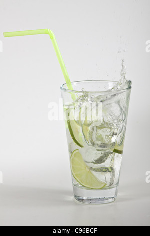 Ice cubes falling into a glass with water and lime Stock Photo