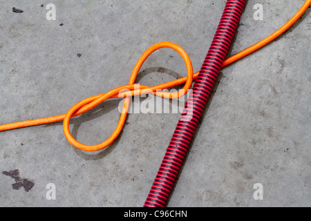 An orange electric flex with a knot in it crossed by a red and black striped plastic hose or conduit Stock Photo