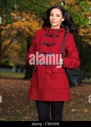 Beautiful young woman walking along the street in fall nature wearing a red coat Stock Photo