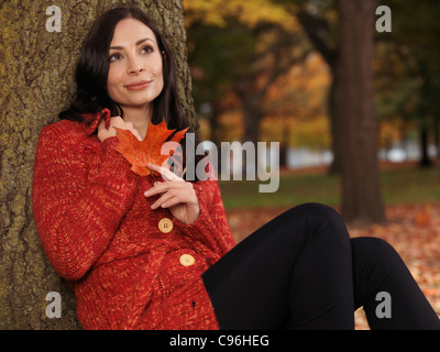 Beautiful smiling woman with daydreaming expression cuddling up in a red sweater in fall nature Stock Photo