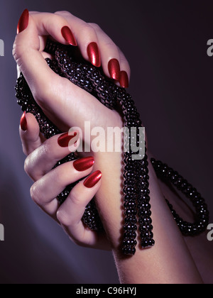 Woman hands with shiny red nails holding jewellery, black necklace Stock Photo