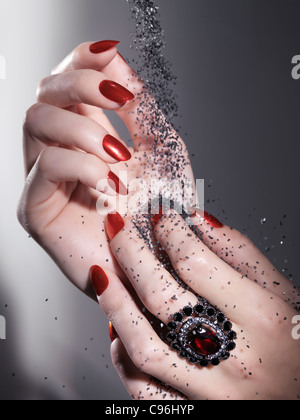 License available at MaximImages.com Black sand falling on woman's hands with bright red nail polish and a red stone ring Stock Photo