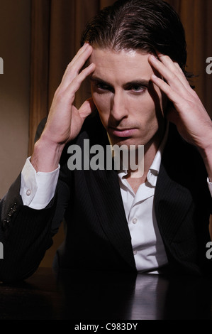 Expressive portrait of a stressed business man sitting at a desk and rubbing his temples Stock Photo