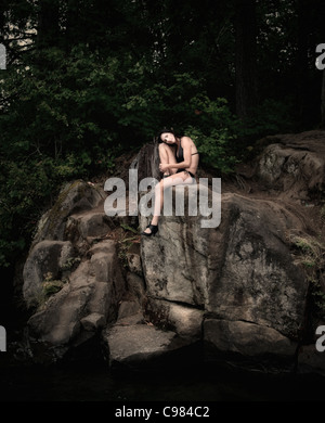 Beautiful woman in bathing suit sitting on rocks over a lake. Stock Photo