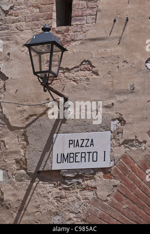 A street lamp attached to a stucco and brick wall casts a long shadow midday in Panicale, Italy. Stock Photo