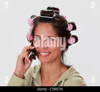 Portrait of a smiling young woman with hair curlers using a mobile phone. Stock Photo