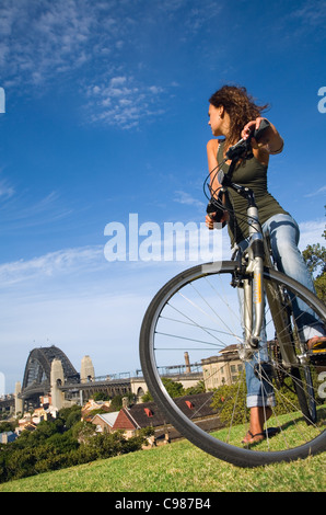 Woman with bicycle at Observatory Hill with Sydney Harbour Bridge in background. The Rocks, Sydney, New South Wales, Australia Stock Photo