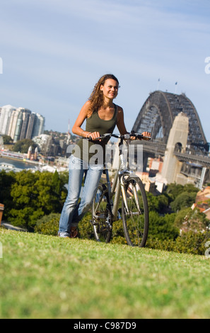 Woman with bicycle at Observatory Hill with Sydney Harbour Bridge in background. The Rocks, Sydney, New South Wales, Australia Stock Photo