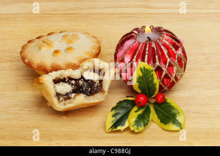 Mince pies with a burning decorative candle and a sprig of fresh variegated holly on a wooden board Stock Photo
