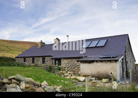 Remote rural cottage with solar panels on roof for heating hot water and generating electricity with small wind turbine spinning Stock Photo