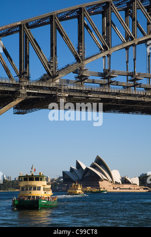 A Sydney ferry cruises under the Harbour Bridge with the Opera House beyond. Sydney, New South Wales, Australia Stock Photo