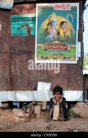 Poor Indian nomadic beggar girl sitting against a hut eating a biscuit. Andhra Pradesh, India Stock Photo