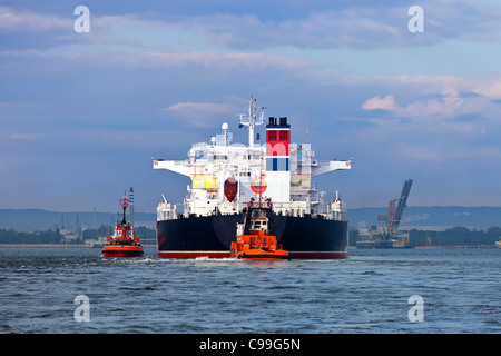 Maneuvers at sea on a cloudy day - Escorting tanker by tugs. Stock Photo