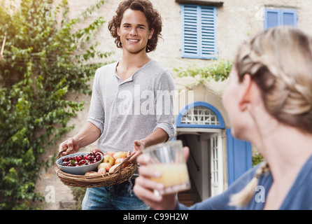 Italy, Tuscany, Magliano, Young man holding basket with apples and cherries with woman in foreground, smiling Stock Photo