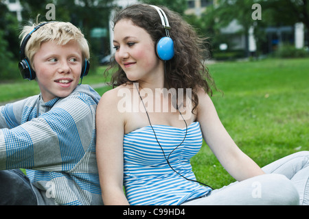 Germany, Berlin, Teenage couple with headphones listening music in park