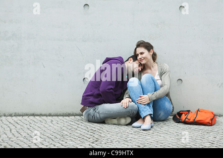 Germany, Berlin, Couple sitting in front of large wall on sidewalk Stock Photo