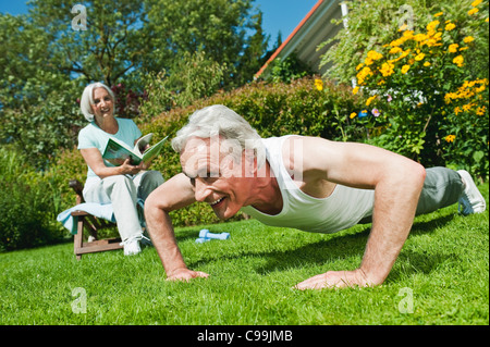 Germany, Bavaria, Man exercising and woman reading magazine in garden, smiling Stock Photo