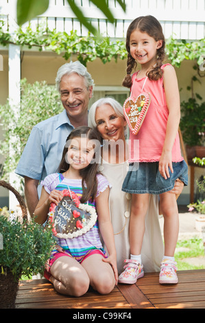 Germany, Bavaria, Grandparents with granddaughter holding gingerbread, smiling Stock Photo