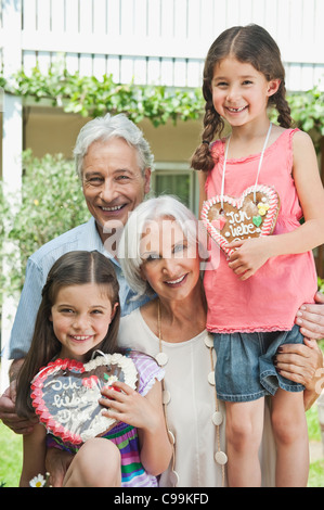 Germany, Bavaria, Grandparents with granddaughter holding gingerbread, smiling, portrait Stock Photo