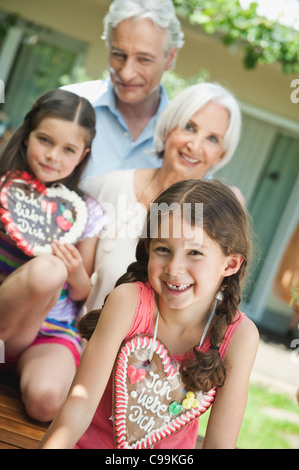 Germany, Bavaria, Grandparents with granddaughter holding gingerbread, smiling Stock Photo