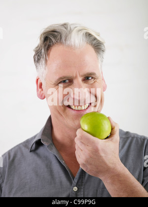 Germany, Hamburg, Senior man holding apple, smiling, portrait Stock Photo