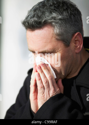 Germany, Hamburg, Mature man blowing nose with tissue, close-up
