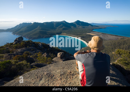 A man looks out over Wineglass Bay from the summit of Mt Amos.  Freycinet National Park, Tasmania, Australia Stock Photo