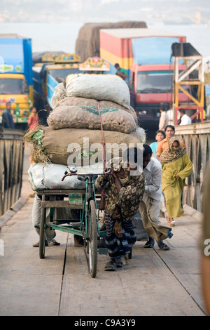 A rickshaw driver pulls his heavy load up the gangplank after disembarking from a ferry Chittaging Bangladesh Stock Photo