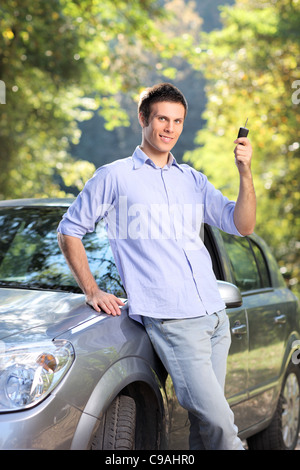A male holding a car key posing next to his automobile Stock Photo