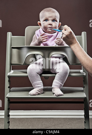 Four month old Baby Girl Eating First Food in Highchair Stock Photo