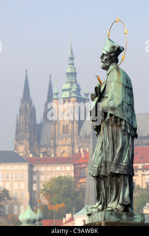 Prague, Czech Republic. Statue of St John Nepomuk on Charles Bridge. Castle and St Vitus Cathedral behind Stock Photo