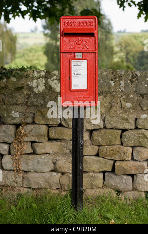 Close-up front view of bright red post box (lamp box style, marked ER) standing in front of drystone wall - Leathley, North Yorkshire, England, UK. Stock Photo
