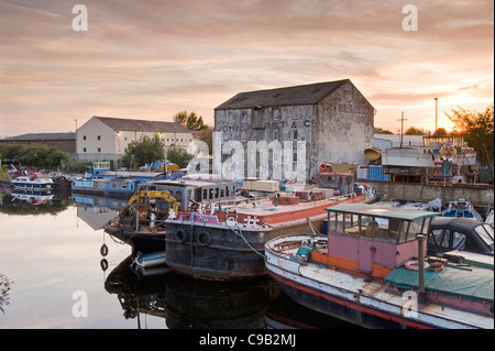 Boats (dilapidated, in need of repair) moored at River Calder boatyard by old rundown industrial mill building, sunset - Wakefield, Yorkshire, England Stock Photo