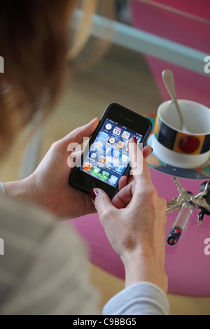 close-up of woman's hand using iPhone 4 smart phone apps, with glass tabletop, keys & cup, studio shoot, UK home. Stock Photo