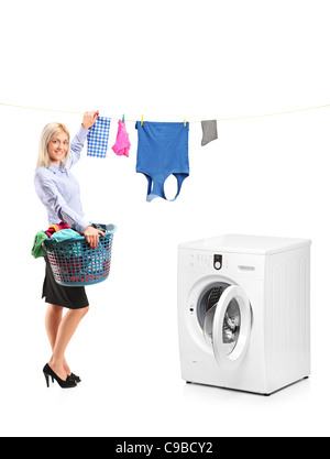 Young smiling woman hanging clothes on clothes line next to a washing machine Stock Photo