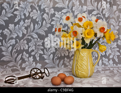 Still life spring Daffodil flowers in vase, vintage pitcher, pots,antique eggbeater cooking utensil, 3 brown eggs, white lace Colourful baking tools Stock Photo