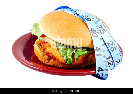 Fried chicken sandwich with lettuce, tomato, and provolone on a bun on a plate surrounded by a measuring tape. Stock Photo