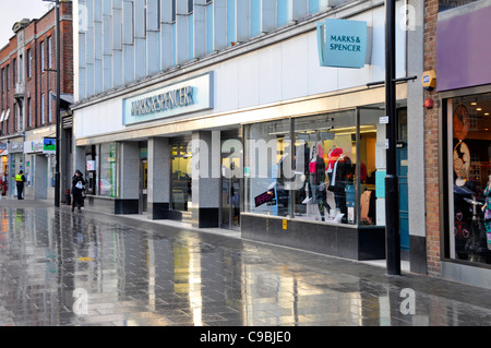 Marks & Spencer shopping High Street store shop window pavement reflections on a rainy January winters day Essex England UK Stock Photo