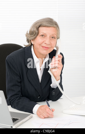 Smiling successful senior businesswoman sitting behind office table portrait Stock Photo