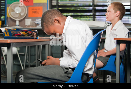 Boy using mobile phone under desk in classroom, Johannesburg, Gauteng Province, South Africa Stock Photo