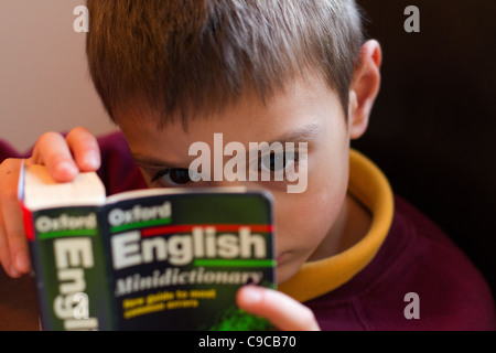 Child reading an oxford English Dictionary in School uniform home schooling during the Corona virus. Stock Photo
