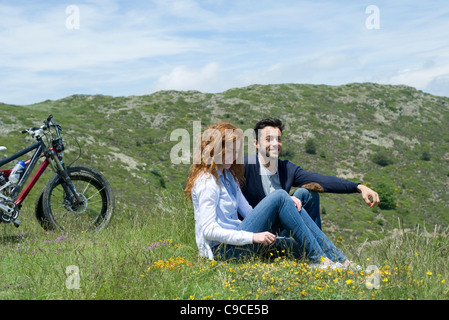 Couple sitting on meadow by mountain bikes Stock Photo