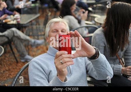 Male tourist using red Apple Iphone to take photograph in Central Park Manhattan New York NYC USA America Stock Photo