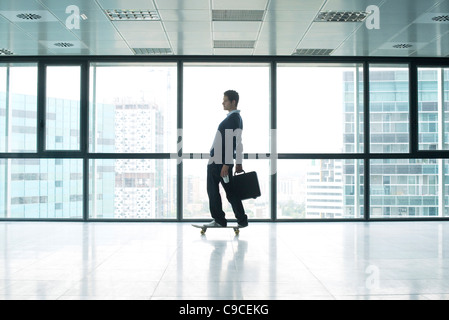Businessman standing on skateboard with briefcase Stock Photo