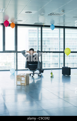 Businessman sitting in new office with balloons and box