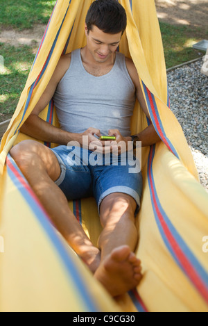 Man relaxing in hammock, text messaging with cell phone Stock Photo