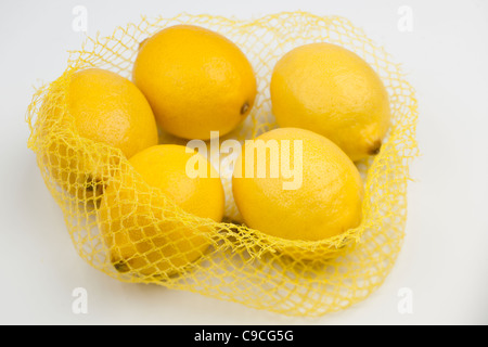 Fresh citrus in mesh bag on beige background. Lemons and limes in